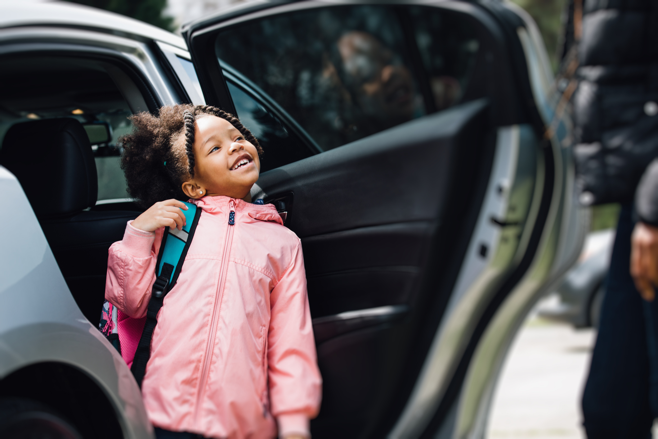 Girl opening parked car door looking at parent with a smile