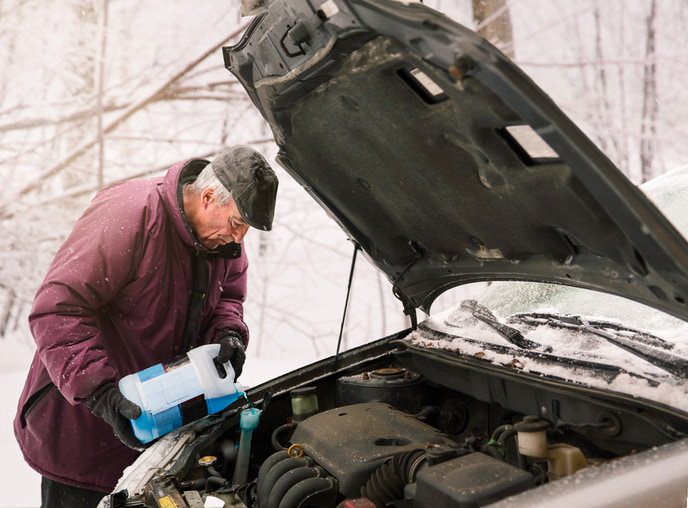 Senior white man pouring windshield wiper fluid in car in a snowy background